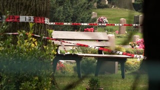 Polizei-Absperrband hängt vor einer Bank auf einem Friedhof.