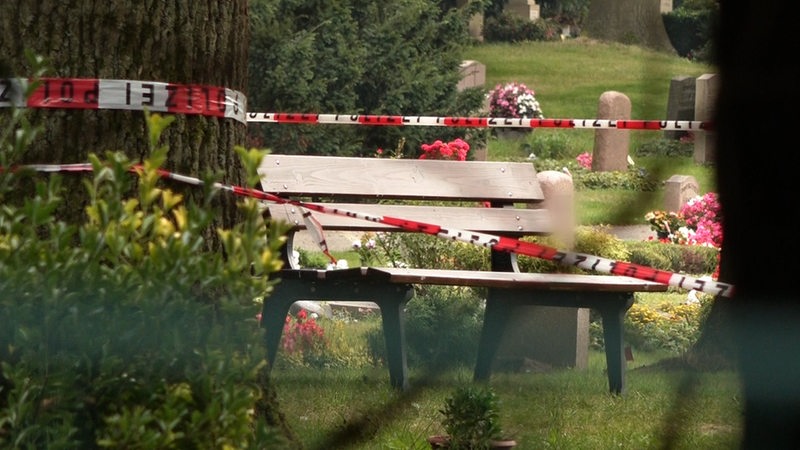 Polizei-Absperrband hängt vor einer Bank auf einem Friedhof.