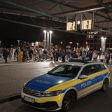 Ein Polizeiauto steht vor einer Menschenmenge an einem Bahnhof