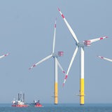 Mehrere Windräder stehen im Meer, dazwischen liegt ein Schiff.