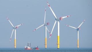 Mehrere Windräder stehen im Meer, dazwischen liegt ein Schiff.