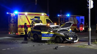 Ein Rettungswagen steht hinter einem zerstörten Polizeiauto