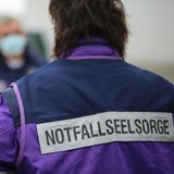 Eine Mitarbeiterin der Notfallseelsorge in Uniformjacke ist von hinten zu sehen.