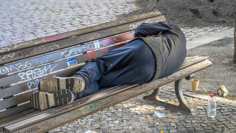 Ein Obdachloser schläft auf einer Parkbank in der Stadt.