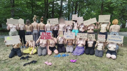 Mehrere Frauen sitzen und stehen "oben ohne" im Horner Bad. Einige halten Plakate vor ihre Gesichter.