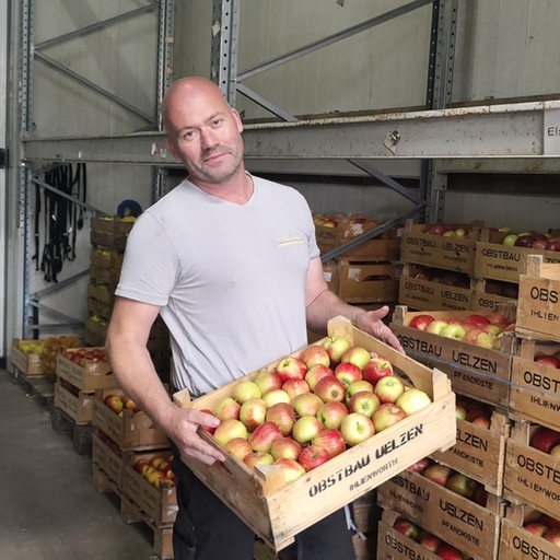 Der Obstbauer Julian Uelzen hebt einen Kasten mit Äpfeln hoch.