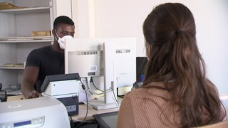 Ein Mitarbeiter des öffentlichen Dienstes mit einer Kundin in seinem Büro am Schreibtisch.