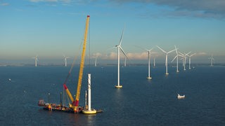 Ein Kran baut eine Offshore-Windkraftanlage zusammen.