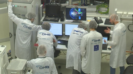 Es sind mehrere Angestellte des Raumfahrtsunternehmen OHB beim arbeiten in weißen Kitteln zu sehen.