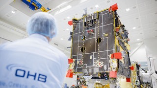 Ein Mitarbeiter von OHB steht vor einem Satelliten