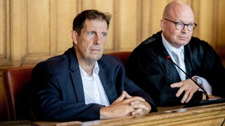 Ein Mann sitzt auf der Anklagebank eines Gerichts. Neben ihm sein Anwalt. 