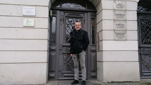 Ein Mann steht vor einer grauen Eingangstür.