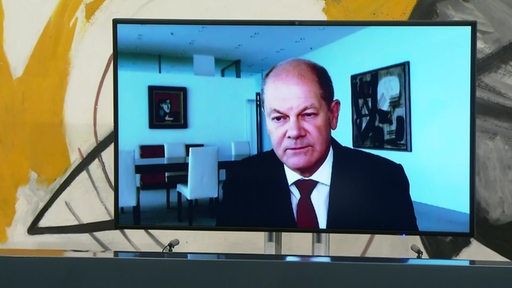 Olaf Scholz ist zugeschaltet durch eine Videokonferenz auf einem Bildschirm zu sehen.