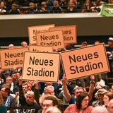 Gäste halten Schilder mit der Aufschrift "Neues Stadion" hoch 