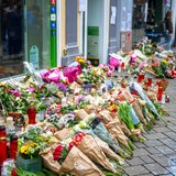 Viele Blumensträuße und Grabkerzen stehen in einer Fußgängerzone.