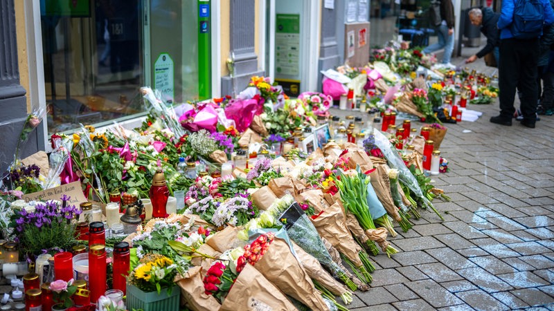 Viele Blumensträuße und Grabkerzen stehen in einer Fußgängerzone.