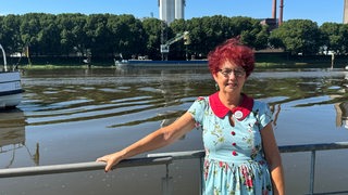 Liselotte Warnecke steht in einem blauen Kleid an einem Geländer vor der Weser und lächelt.