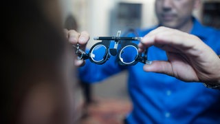 Ein Optiker hält eine Probebrille in der Hand.