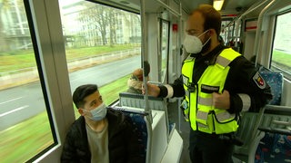 Ein Ordnungsamt-Mitarbeiter kontrolliert eine Person in der Bahn.