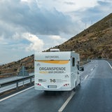 Ein weißer Camper mit der Aufschrift "Organspende Reden wir drüber" fährt auf einer Straße.