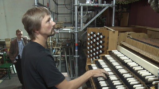 Ein Mann sitzt vor einer Orgel und spielt sie an.