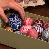Eine Hand legt verzierte Eier in eine Schale.
