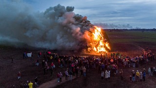 Aus der Ferne ist zu sehen, wie ein Osterfeuer unter großer Rauchentwicklung abbrennt. 