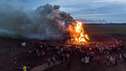 Aus der Ferne ist zu sehen, wie ein Osterfeuer unter großer Rauchentwicklung abbrennt. 