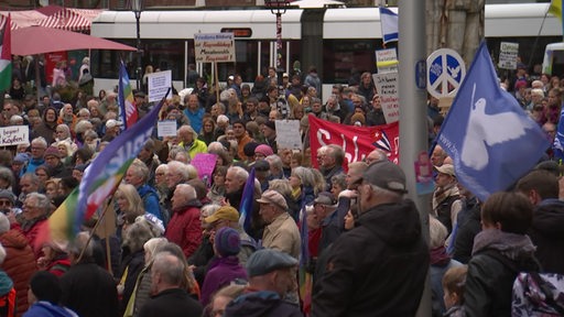 Teilnehmer eines Ostermarsches mit Flaggen und Schildern, im Hintergrund eine Straßenbahn