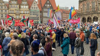 Menschen demonstrieren mit transparenten und Flaggen auf dem Bremer Marktplatz