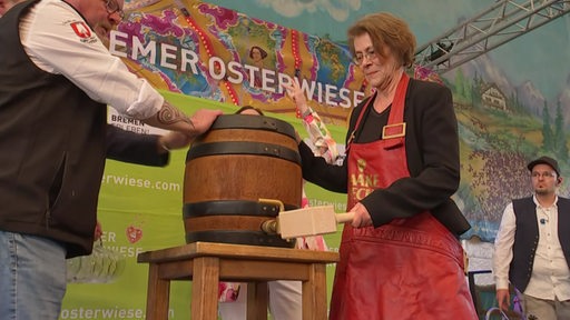 Zwei Personen halten ein Bierfass fest, der Anstich wird mit einem großen Holzhammer gemacht