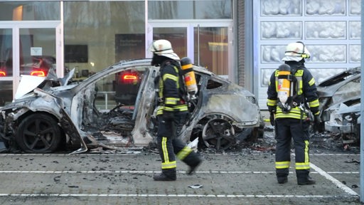 Zwei Feuerwehrmänner vor einem ausgebrannten Tesla