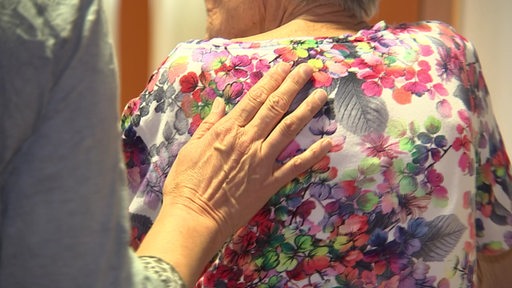 Eine Frau legt einer älteren Frau die Hand auf den Rücken.