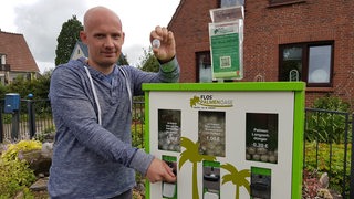 Erfinder Florian Faust steht neben einem grün-weißen Saatgut-Automaten im Vorgarten