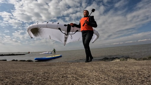 Ein Kitesurfer trägt sein Kite am Strand