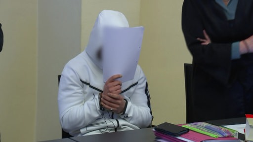 Angeklagter versteckt sein Gesicht hinter Papieren.