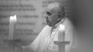 Ein schwarz-weiß-Bild, auf dem Papst Franziskus zwischen Kerzen zu sehen ist.