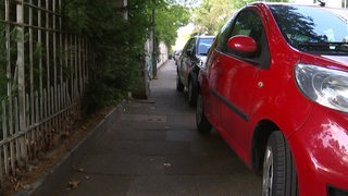 Ein Bürgersteig, auf dem Autos halb parken und somit den Durchgang schmaler machen.