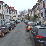 Viele Autos stehen in einer Straße aufgesetzt auf dem Gehweg geparkt.