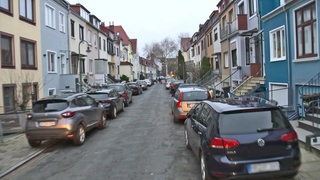Viele Autos stehen in einer Straße aufgesetzt auf dem Gehweg geparkt.