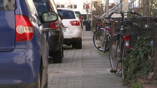 Eine Reihe Autos, die auf einem Bordstein parken und den Gehweg verengen.