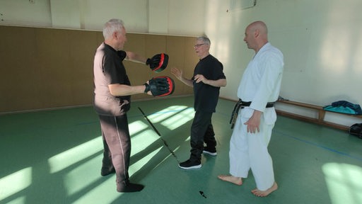 Ein Mensch in Karate-Dress schaut zwei Personen beimTraining zu.