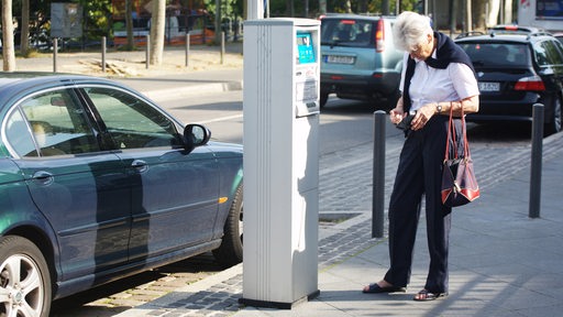 Eine Frau sucht in ihrer Börse nach Kleingeld, um an einem Parkscheinautomaten einen Parkschein für ihr Auto zu ziehen