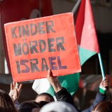 Eine Person hält auf einer Demonstration ein Schild in die Höhe. Auf dem steht: "Kinder Mörder Israel."