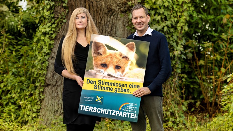 Zwei Mitglieder der Partei Mensch Umwelt Tierschutz halten ihr Wahlplakat.