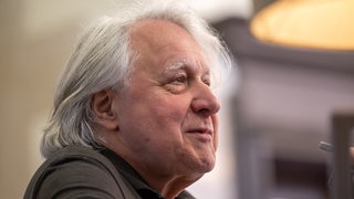 Ein älterer Mann mit schulterlangen weißen Haaren im Profil.