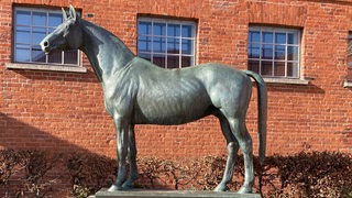 Eine Pferdeskulptur aus Bronze steht vor einem Haus.