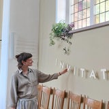 Eine Frau steht neben einer Fensterbank mit Pflanzen und hält eine Girlande.