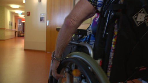 Eine alte Dame fährt in ihrem Rollstuhl durch den Flur eines Altersheimes.