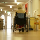 Eine Seniorin rollt mit ihrem Rollstuhl durch den Flur einer Pflegeeinrichtung.